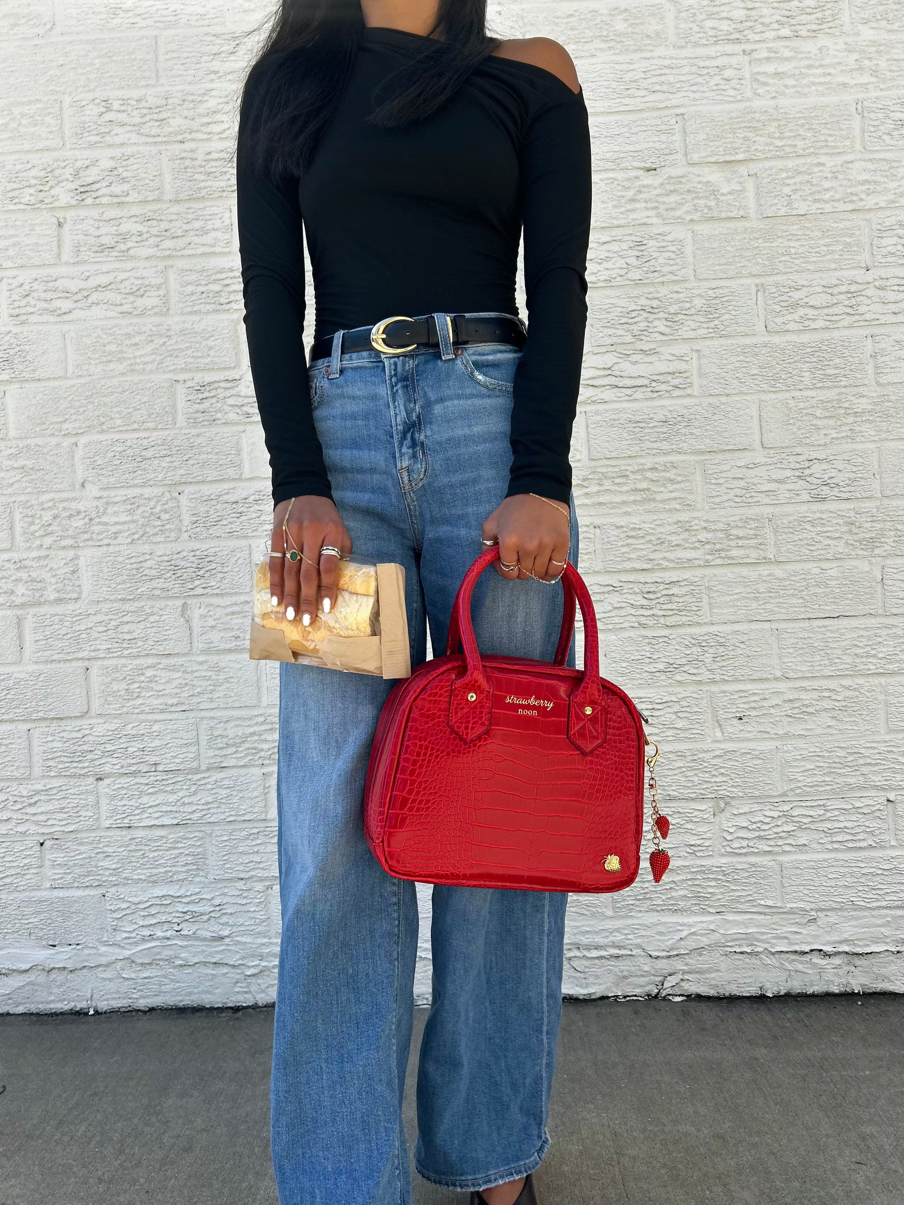 Person holding a red handbag and beige clutch against a white brick wall.